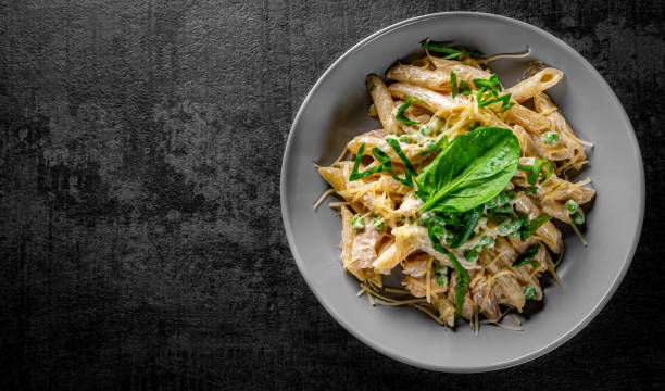 pasta de penne con carne de pollo, salsa de crema y queso en un tazón sobre fondo de pizarra negra gris oscuro - noodles pasta chicken breast color image fotografías e imágenes de stock