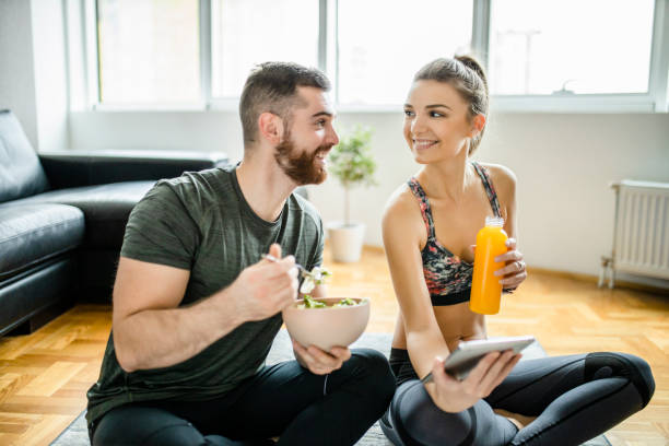 Happy couple using digital tablet and eating snack after intensive home workout