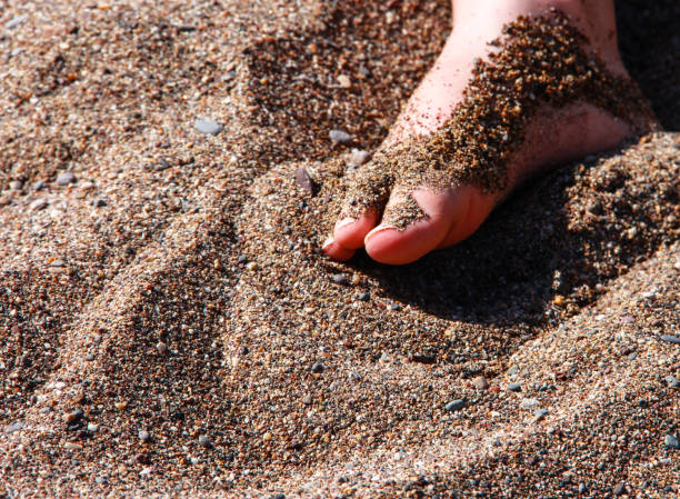 istock A child's foot in the sand. Background with dark sand. 1289718527