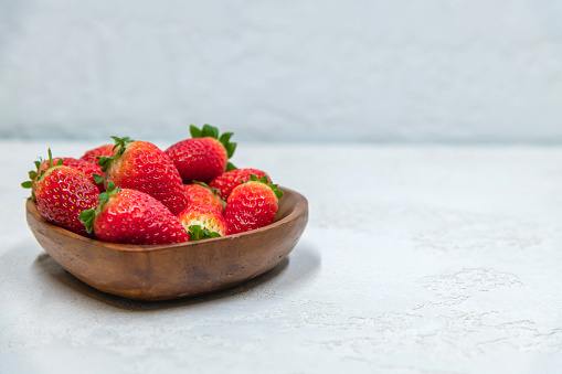 Fresh red strawberries in wooden bowl side view. Strawberry fruits on gray concrete background. Copy space for your text. Organic food theme.