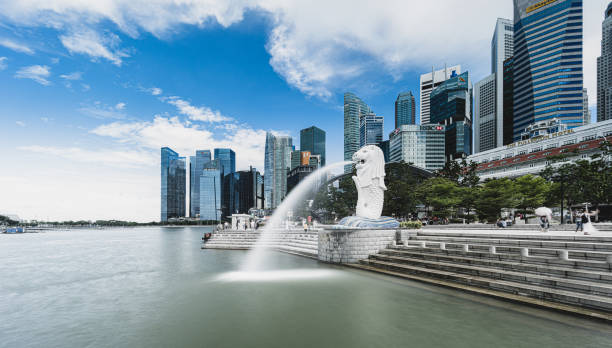 Aerial view of the Merlion monument and the Singapore skyline a sunny day Singapore, June 14, 2019. Aerial view of the skyline of Singapore during a beautiful sunny day with the financial district in the distance. In front people are visiting the famous Merlion fountain at Marina Bay. Singapore is located in Southeast Asia. business architecture blue people stock pictures, royalty-free photos & images