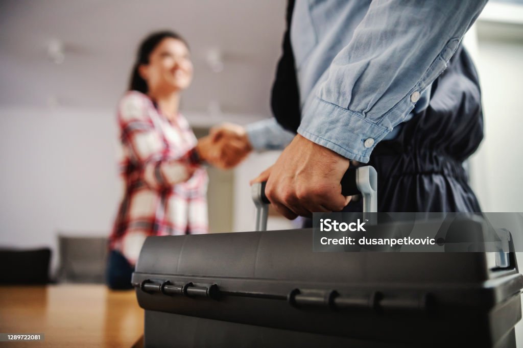 Nurse sitting at home, holding syringe with cure and giving advices over internet. Woman shaking hands with a repairman while standing at home. Plumber Stock Photo