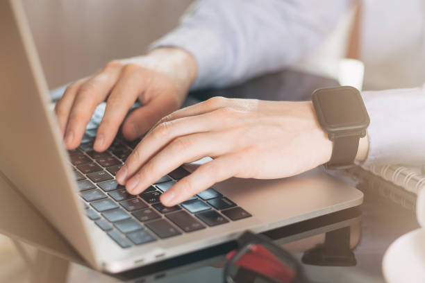 Cropped image of a young man working on his laptop, man hands busy using laptop at office desk, young male student typing on computer sitting at black table. Young businessman working with laptop at office Cropped image of a young man working on his laptop, man hands busy using laptop at office desk, young male student typing on computer sitting at black table. Young businessman working with laptop at office raincoat stock pictures, royalty-free photos & images