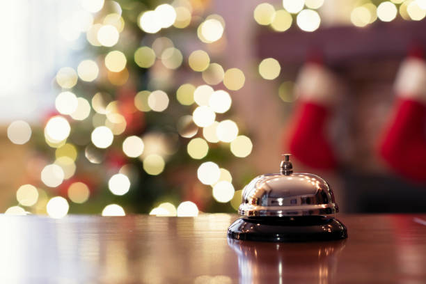 christmas travel. silver vintage bell on reception desk of guesthouse  and color shining garland on christmas tree on background. hotel, restaurant. - service bell fotos imagens e fotografias de stock