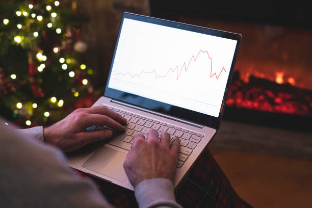 istock Man freelancer in santa claus hat working on laptop with graphs and charts on screen sitting near christmas tree and fireplace. 1289724821