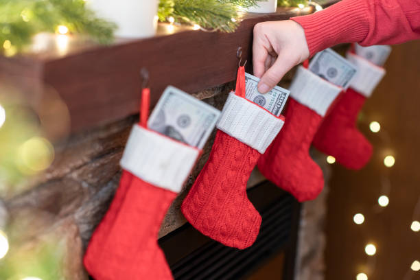 Woman putting american dollars in hristmas red socks for gifts on the fireplace in bokeh lights. stock photo