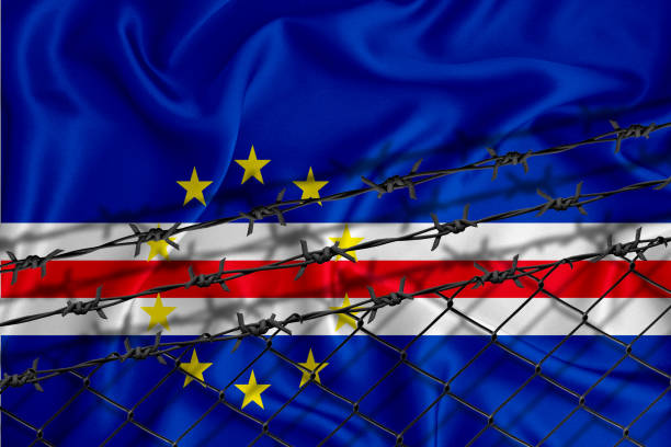 istock Cabo Verde flag development, fence mesh and barbed wire. Emigrants isolation concept. With place for your text. 1289726386