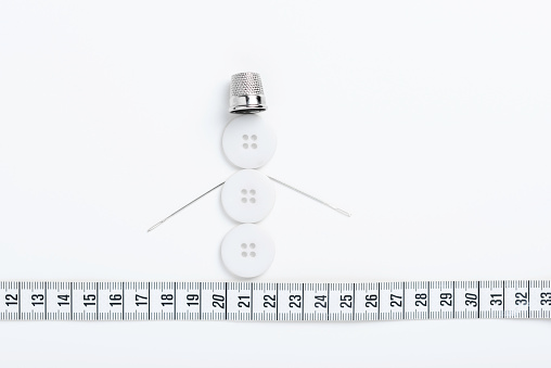 Sewing theme creative flat lay design: snowman made of buttons, thimble, needles