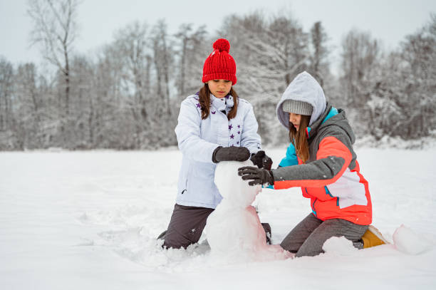 istock Two girls making a snowman in a winter time 1289733019