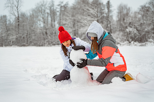 Two young girls making a snowman in a winter time in nature.