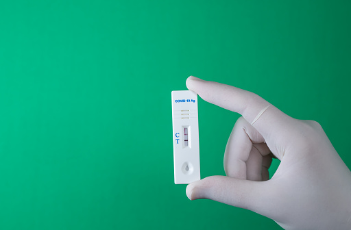 Rapid antigen COVID-19 test. Quick rapid diagnostic test with positive results. Hand holds antigen test on green screen. copy space.