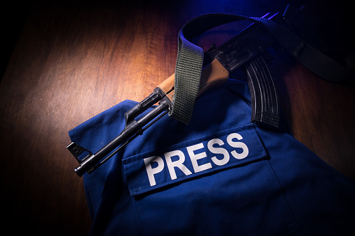 Media Journalism at risk concept. Blue journalist (press) vest in dark with backlight and fog. Weapon on journalist vest. Selective focus