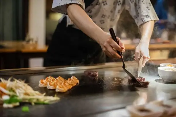 teppan show at a traditional Japanese restaurant. hands of the cook. Japanese cook prepares meat, fish, rice, vegetables for guests