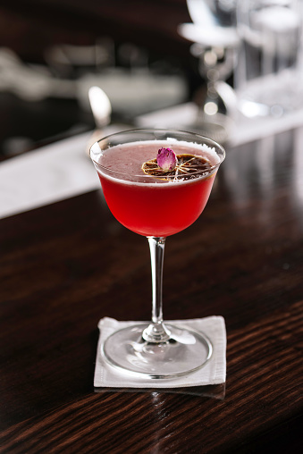 Decorated alcohol cocktail with a rose flower and slice of lemon on bar counter. Cosmopolitan cocktail.