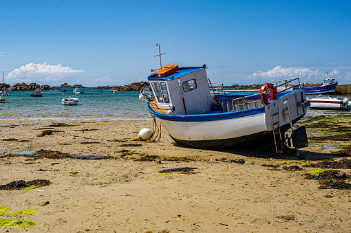 Breton landscape in summer. A fishing boat stranded on the sand at low tide. Sand beach strewn with seaweed.