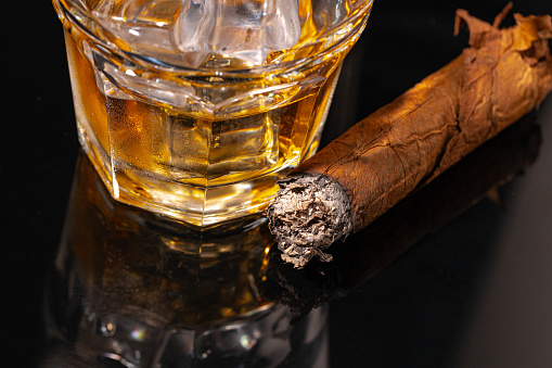 Glass of whisky and lighted cigar on black background close up