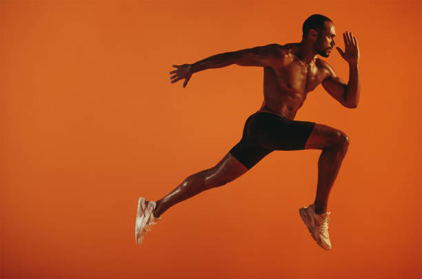 istock Muscular athlete running on orange background 1289749905