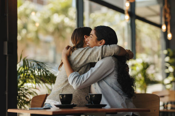 Two female friends meeting in a cafe Two female friends meeting in a cafe. Women sitting together at a cafe giving each other a hug. female friendship stock pictures, royalty-free photos & images