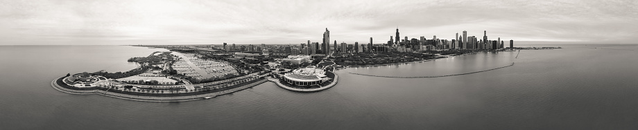 Incredible black and white wide angle Chicago city skyline aerial panorama over Lake Michigan with highrise skyscraper buildings and boat harbors along the horizon with a beautiful cloudy sky above.