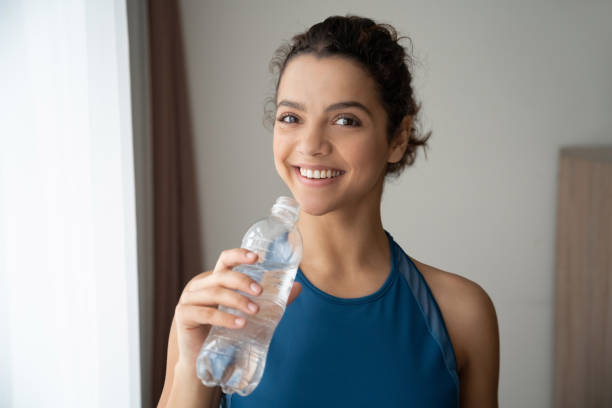retrato de cerca de hermosa joven y sonriente mujer en forma beber agua en casa. - aerobics beautiful bottle body fotografías e imágenes de stock