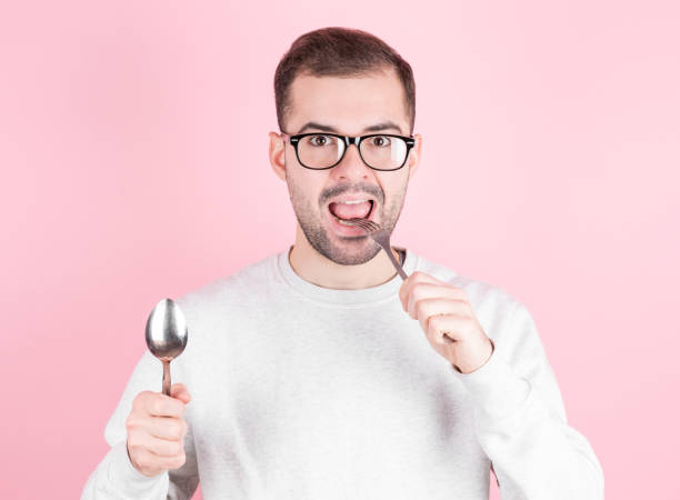 Hungry man licks his lips while holding a fork and spoon in his hands. The concept of diet, food intake and hunger.