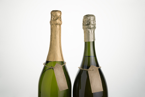Two clear bottles of sparkling wine on a light background. Horizontal orientation. Side view.