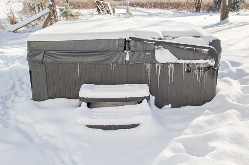 Covered outdoor hot tub surrounded by snow and with hanging ice. Winter background.