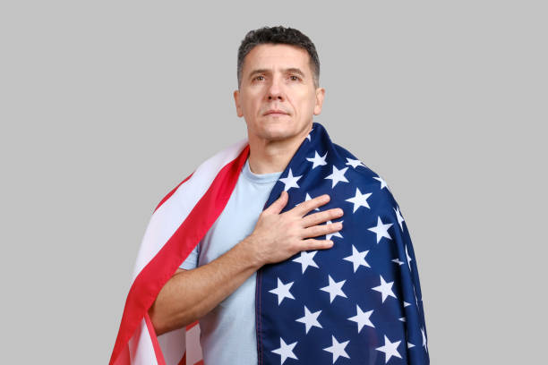 istock Handsome middle-aged man covered with American flag puts hand on his heart 1289758832