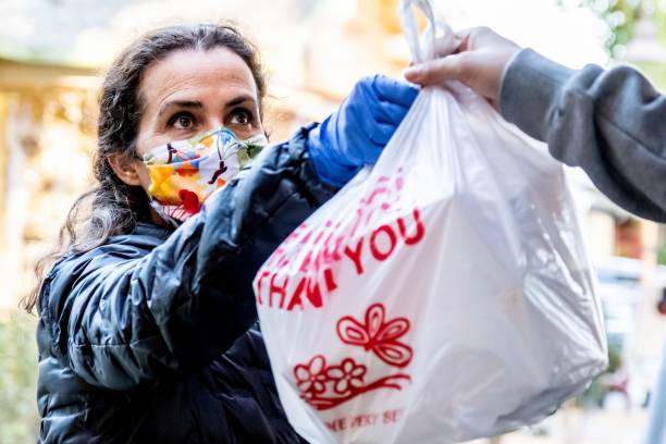 mujer madura desempleada que recibe comida gratis del centro de caridad usando una máscara protectora para la cara - alimentar fotos fotografías e imágenes de stock