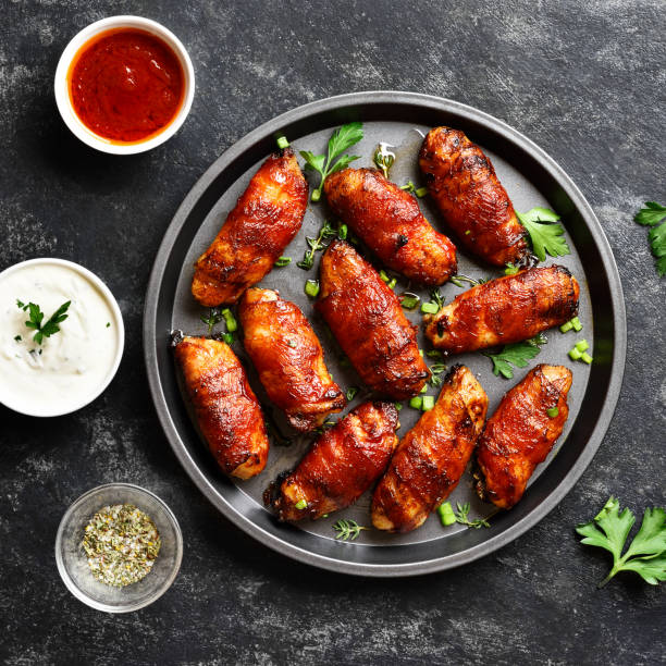 Close up view of bacon wrapped grilled chicken wings Bacon wrapped grilled chicken wings on plate over dark stone background. Tasty snack from chicken meat, bacon in sweet, sour, salty and spicy sauce. Top view, flat lay bacon wrapped stock pictures, royalty-free photos & images