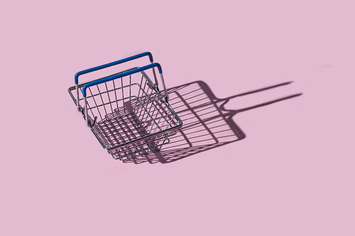 Empty metal shopping basket on a pastel pink background with copy space. Top view.