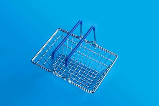 Empty metal shopping basket on a light blue background with copy space. Top view.