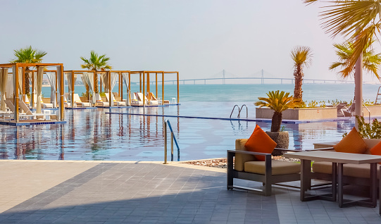 Dubai, UAEmirates - October 5, 2019. Beautiful luxurious pool on the resort overlooking the sea and the bridge. Modern design, white deckchairs, palm trees