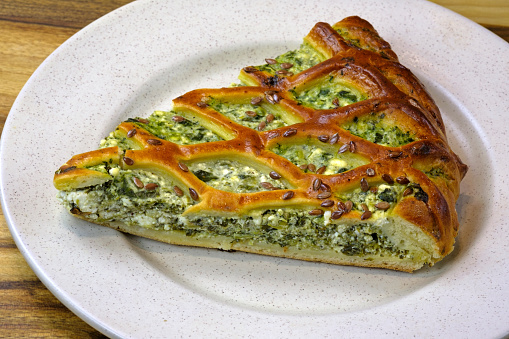 A slice of cottage cheese and spinach pie on a plate. Delicious homemade pie stuffed with spinach. Homemade cakes with cottage cheese and herbs.
