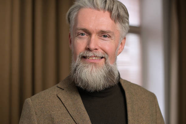 istock Stylish gray-haired man with a beard in a jacket looks confidently 1289773747