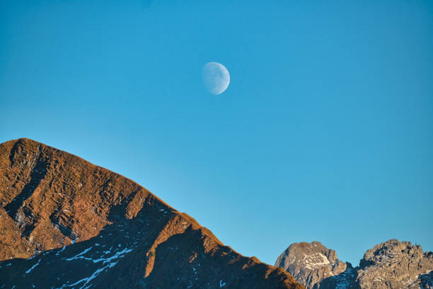 Chamonix, France - October 31, 2017. View of the moon in a pure high mountain sky. in the foreground, a mountain peak covered with rocks and snow is visible. in the background, in a night sky, the crescent moon is visible.