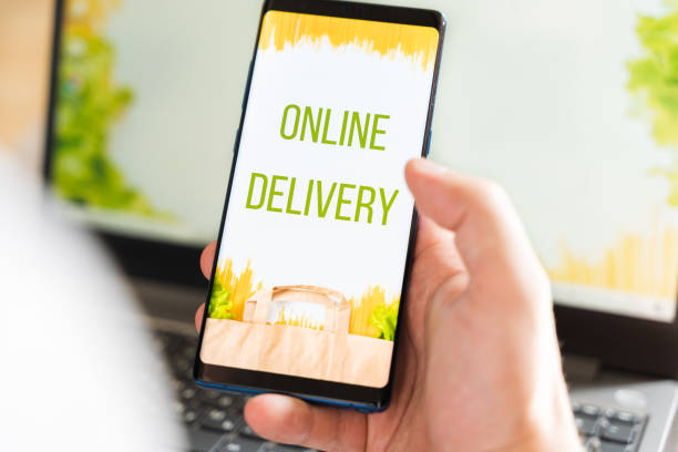 istock Hand with mobile phone. Online internet shopping, order through mobile application. Laptop. Home delivery of food, groceries from grocery store. Paper bag with pasta on screen. Payment by credit card 1289796811