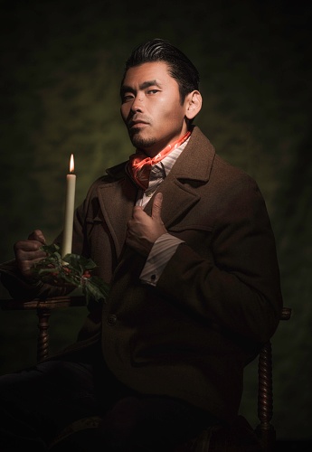 This image is a painterly style victorian portrait of a a well dressed asian man, holding an antique burning candle and fixing his suit as he looks towards the viewer.