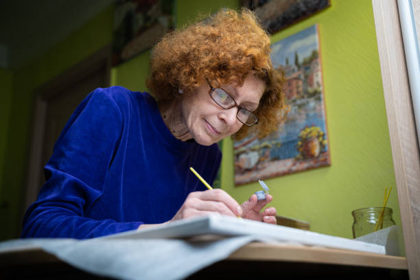 istock Age, retirement, creativity, imagination and art. Creative work. Caucasian mature female paints picture on canvas with oil paint and brush at home during quarantine and lockdown coronavirus, covid 19 1289799720