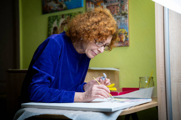 istock Age, retirement, creativity, imagination and art. Creative work. Caucasian mature female paints picture on canvas with oil paint and brush at home during quarantine and lockdown coronavirus, covid 19 1289800755