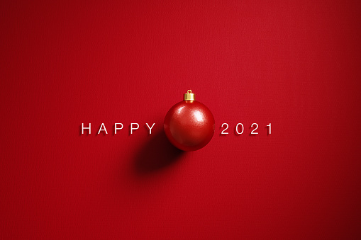 A red Christmas bauble and happy 2021message on red background. Horizontal composition with  copy space. 2021 new year concept.