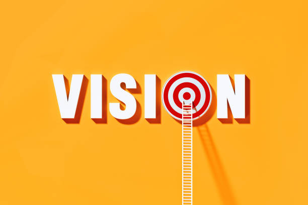 istock White Ladders Leaning on Vision Written  Bull's Eye Target on Yellow Wall 1289805021