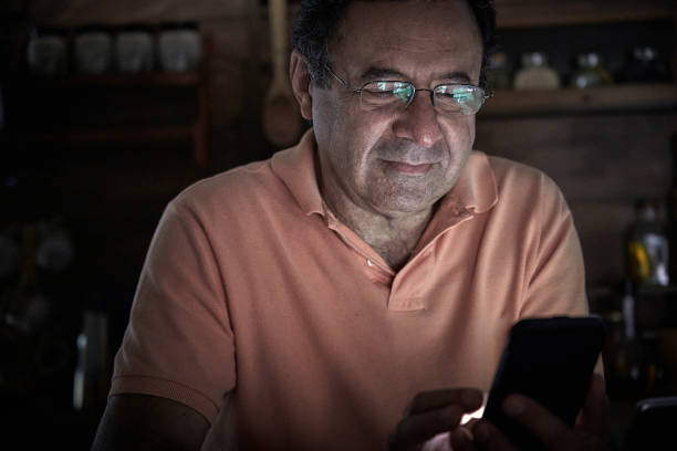 istock Senior Hispanic man using smart phone in a domestic kitchen home office with low lighting 1289806229