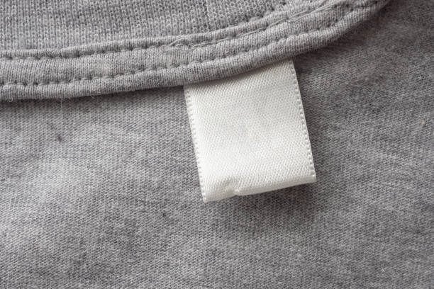 istock Blank white laundry care clothes label on gray fabric texture background 1289811924