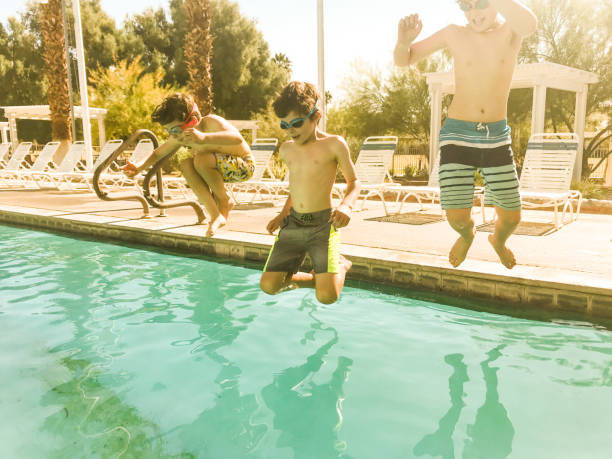 istock Three young boys jump into a pool on a warm and sunny day. 1289812406