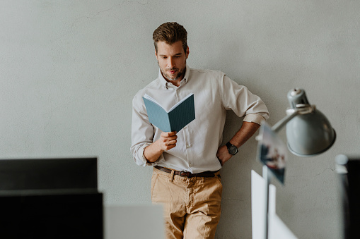 Handsome young businessman wearing a white shirt reading a book
