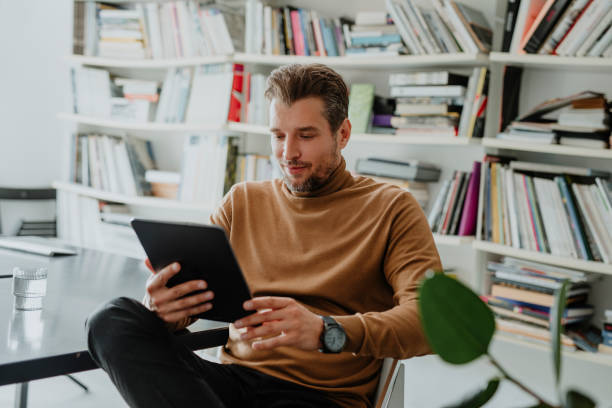 istock Handsome Young Caucasian Man Using a Digital Tablet in his Office/Library 1289815546