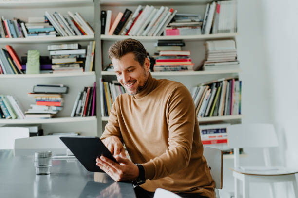 istock Smiling Handsome Freelance Businessman Using a Digital Tablet in his Office/Library 1289815549