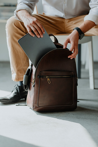Hands of an anonymous businessman putting a tablet computer into a leather backpack