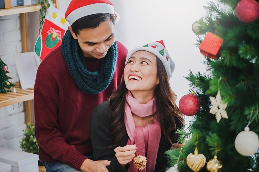 Young Asian couple decorating a Christmas tree in Christmas and Happy New Year holiday festival at home background.Christmas celebration of lover concept.